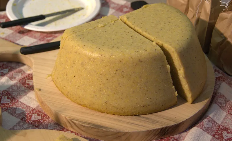 A round of golden polenta turned out onto a wooden board and cut into wedges